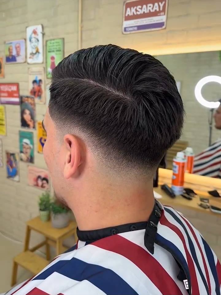 Achterkant van een kort kapsel met fade en scheiding, voor de wand met kapselposters in de studio