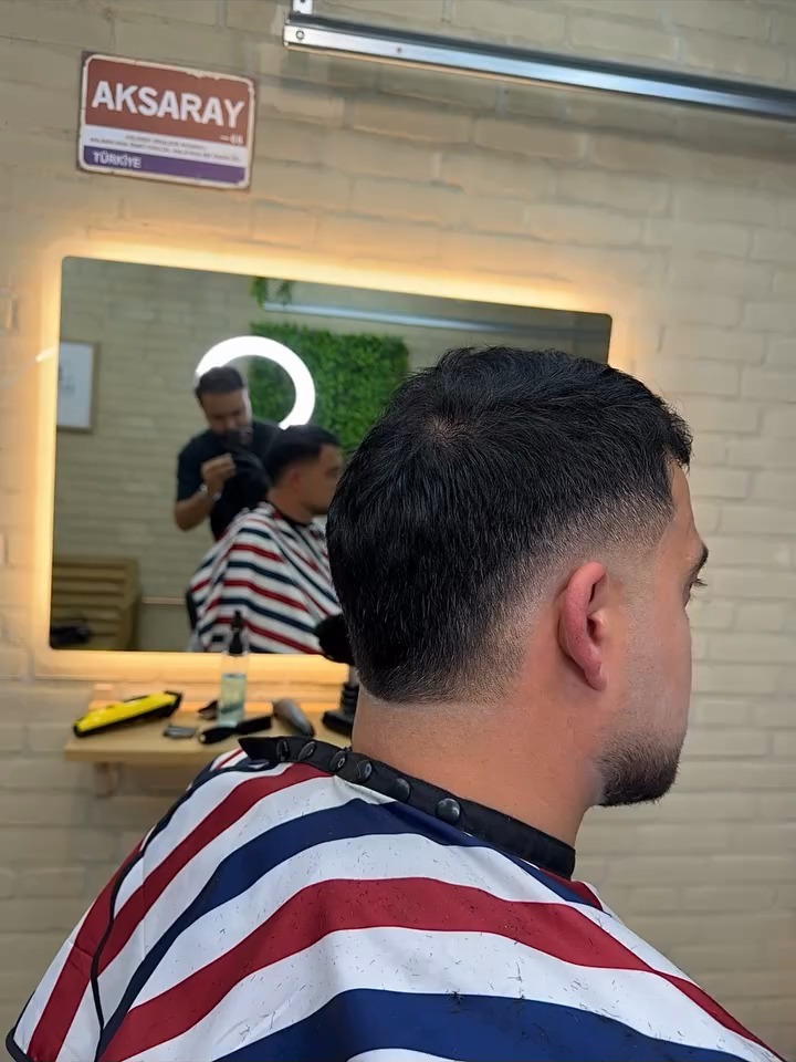 Klant in de stoel met een korte fade, in de spiegel de kapper aan het werk