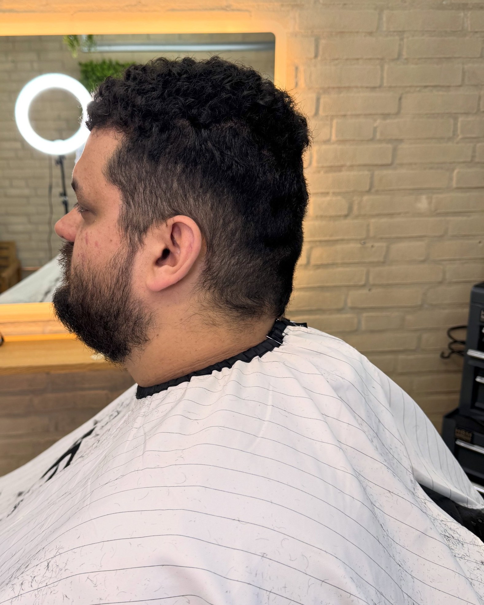 Klant met een volle baard en een fade, in de kapmantel voor de verlichte spiegel